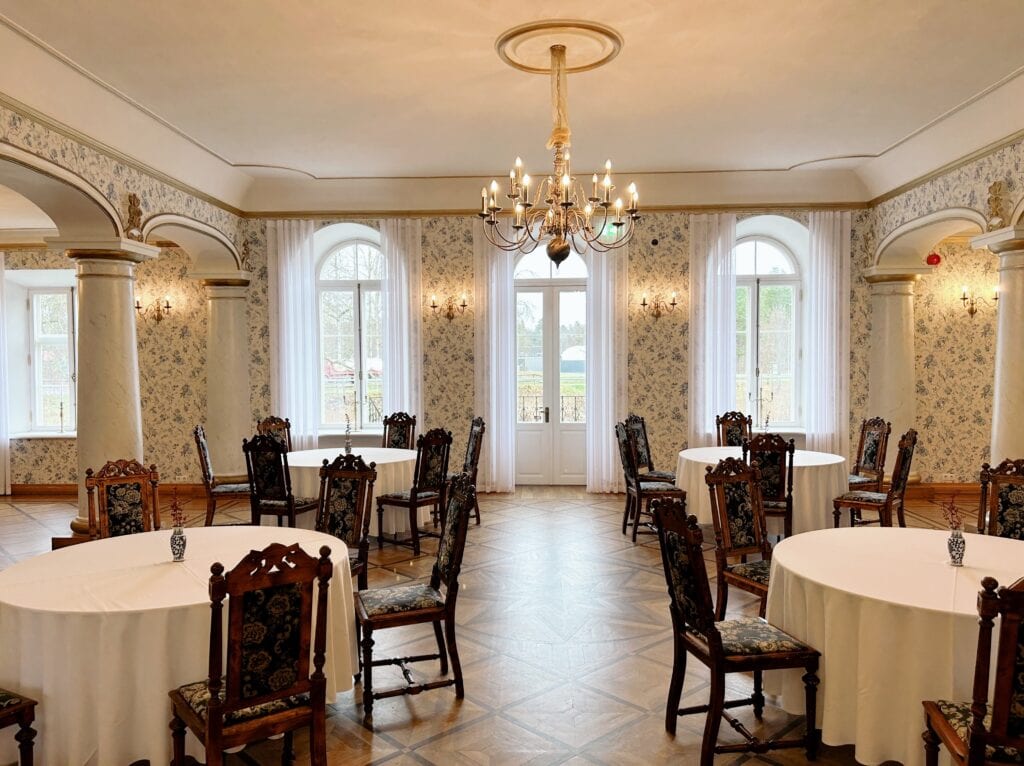 Padise mõisa peosaal ümmarguste laudade ja pruunide mõisatoolidega
