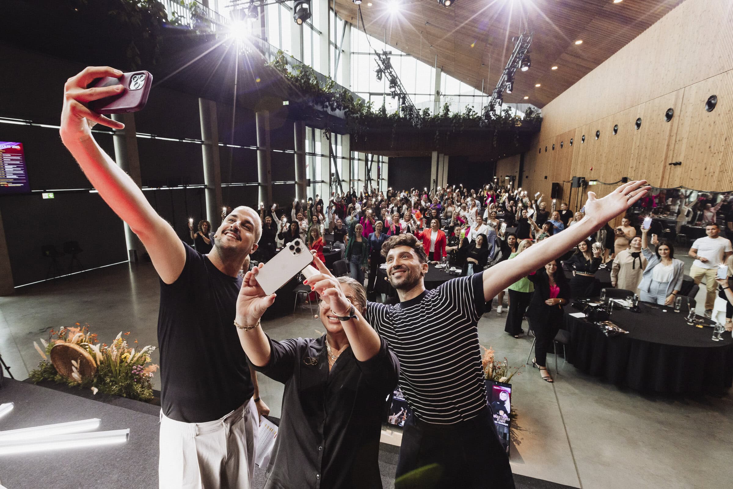 Conference management Three people taking a selfie on stage with all the conference participants