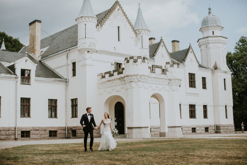 Celebrate Group’s couple, Johanna and Henri, holding hands and posing in front of their wedding venue, Alatskivi Castle.