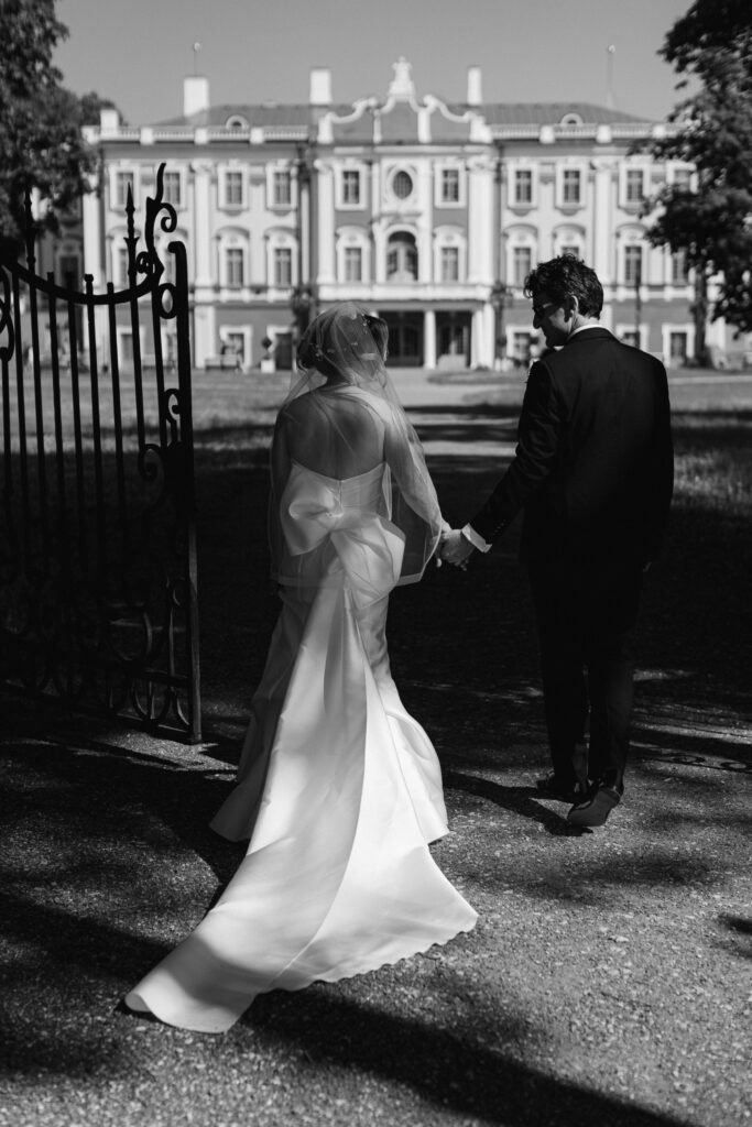 Aili and Eric walking hand in hand toward Kadriorg Castle on their wedding day, organized by Celebrate Group.