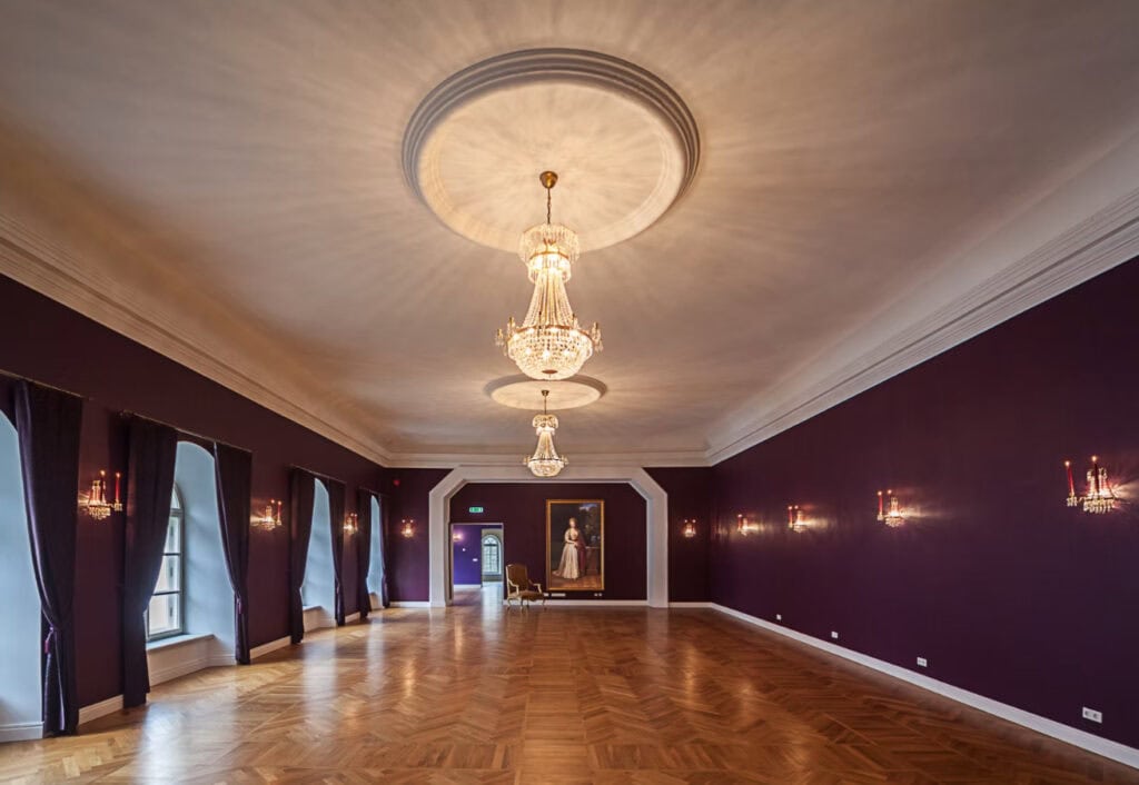 Koluvere Castle’s luxurious hall, adorned with purple walls and sparkling chandeliers.