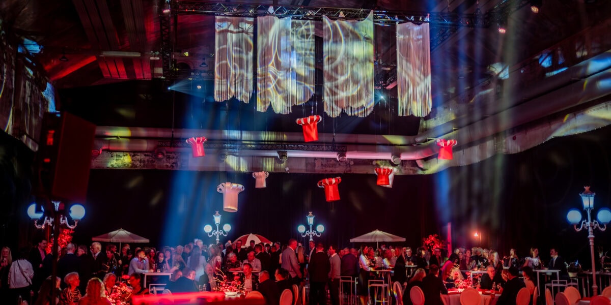 Mamma ja Saarioinen Eesti juubeliüritus Nobeli saalis, kus külalised istuvad laudade taga ning laes ripuvad suured paberist kokamütsid.