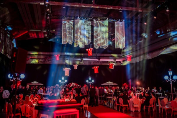 Mamma ja Saarioinen Eesti juubeliüritus Nobeli saalis, kus külalised istuvad laudade taga ning laes ripuvad suured paberist kokamütsid.