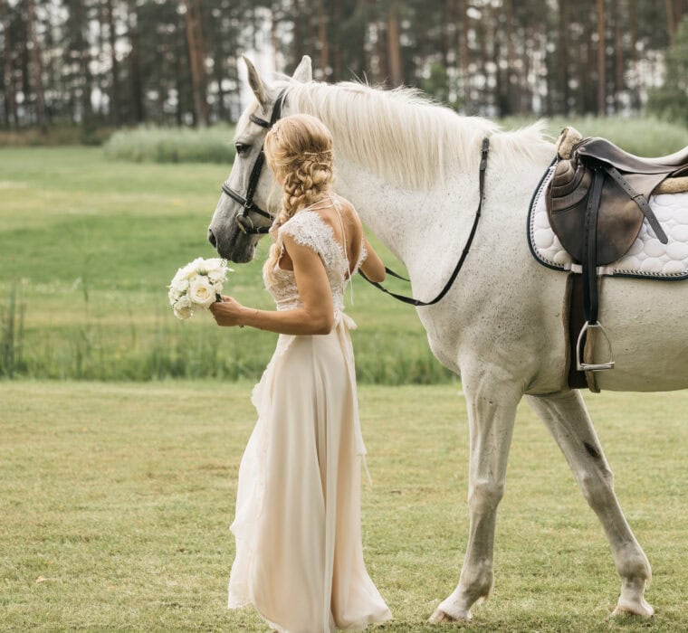 Pruut jalutamas valge hobusega, hoidmas valgete lilledega pruudikimpu.