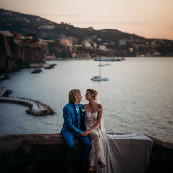 Pruutpaar istub kiviääre peale, Sorrento linn taustal.